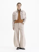 Pantalon de jean color beige, de corte wide leg con silueta redondeada y pinzas en las rodillas. Cuenta con cierre de botón y bragueta, bolsillos laterales y traseros, y detalles de remaches metálicos.