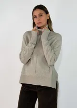 Sweater de punto color beige con cuello alto, manga larga y diseño holgado. Presenta una costura vertical central en el frente, puños y ruedo acanalados, y aberturas laterales en el bajo.