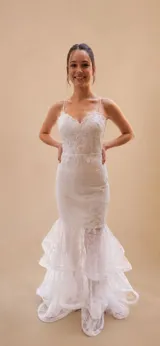 Vestido de novia corte sirena con escote corazón y finos breteles. El cuerpo presenta apliques bordados sobre encaje, mientras que la falda incorpora capas de tul con terminaciones en volados.
