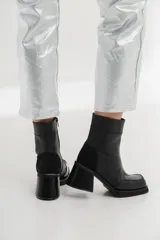 Bota corta de cuero negro con diseño bicolor que combina cuero liso y cuero charol en la puntera. Cuenta con taco cuadrado de altura media y cierre lateral interno.