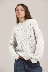 Sweater de punto color blanco con diseño de trenzas y rombos, cuello redondo y detalle de ojales metálicos distribuidos en el frente y las mangas.