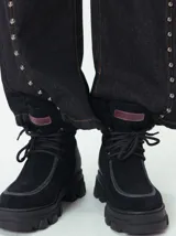 Borcegos de caña baja con diseño robusto, confeccionados en una combinación de gamuza y cuero sintético en tonos verde oliva. Presentan suela track de goma dentada en color suela, cordones al tono con ojalillos amarillos y cuello acolchado para mayor confort.