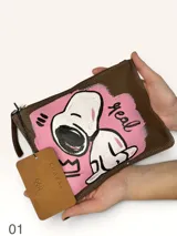 Sobre de cuero marrón con diseño pintado a mano que presenta al personaje Snoopy sobre un fondo rosado y la palabra 'heal'. Cuenta con cierre superior y etiqueta de cuero colgante.