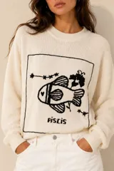 Sweater de tejido de punto color crudo, con cuello redondo y diseño oversize. Presenta un gran bordado artesanal en negro en el frente con motivo del signo Piscis.