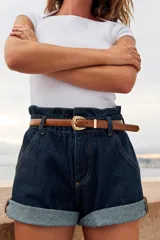 Bermuda baggy de denim azul oscuro con tiro alto, estilo paperbag, cintura elástica y costuras en contraste. Incluye bolsillos delanteros y un cinturón delgado de cuero marrón.