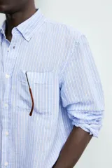 Camisa regular fit de manga larga con diseño a rayas verticales celestes y blancas. Cuenta con cuello abotonado, bolsillo de parche en el pecho y cierre frontal con botones.
