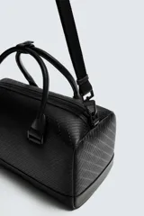 Bolso tipo bowling color negro con textura geométrica en relieve. Tiene doble asa de mano y correa de hombro ajustable y extraíble. El compartimento principal tiene cierre de cremallera y un bolsillo interior con cremallera.
