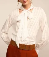 Blusa de crepé color blanco con rayas verticales finas en azul. Tiene cuello con lazo para atar, mangas largas y corte recto.