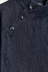 Camisa de denim azul oscuro, de corte cuadrado y manga ancha acampanada. Presenta cuello mao y cierre asimétrico con botones a presión en el frente.