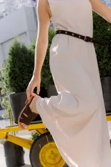 Cinturón de gamuza color marrón con ojales metálicos plateados distribuidos a lo largo de la tira y hebilla metálica de diseño redondeado.