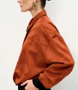 Campera bomber de gamuza sintética color terracota, con cuello clásico, cierre frontal, hombros caídos y puños ajustados.
