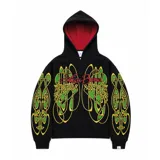 Hoodie oversize de color negro con estampado gráfico en pecho y mangas en tonos amarillos y verdes. Presenta un forro interior de capucha en color rojo con textura tejida y logo bordado en la manga.