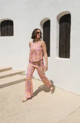 Top sin mangas con cuello redondo, confeccionado en lino con estampado floral en tonos rosados y naranjas. Presenta un diseño con cierre de tres lazos en la espalda.