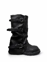 Botas de caña media en color negro, confeccionadas en cuero sintético con acabado mate. Presentan un diseño holgado con tres correas horizontales ajustables mediante hebillas metálicas plateadas y una suela de goma robusta con textura antideslizante.