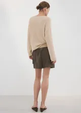 Chaleco de punto grueso color beige, de diseño recto, con cuello en V y manga larga.