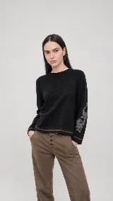 Sweater de lana color beige con calce holgado y cuello redondo. Presenta un bordado negro con diseño de arabescos en una de las mangas y detalles de rayas y puntos en contraste en el ruedo y los puños.