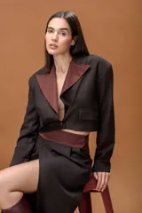 Blazer corto de corte cropped, color marrón oscuro con solapas en contraste de color bordó. Presenta cierre frontal con un botón y bolsillos decorativos en el frente.