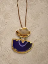 Collar largo con tira de cuero marrón y gran dije colgante compuesto por dos piezas de piedra natural (ágata) en tonos marrón y violeta, engarzadas en metal dorado.