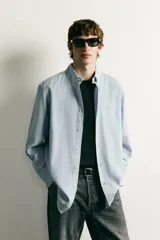 Camisa de corte regular fit confeccionada en algodón, con estampado de cuadros pequeños en tonos celestes. Presenta cuello abotonado, cierre frontal con botones y mangas largas con puños abotonados.