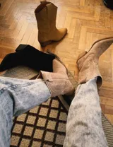 Bota corta de gamuza color marrón topo, estilo western, con bordados decorativos en hilo blanco en caña y empeine. Posee taco cuadrado de madera y punta ligeramente afilada.