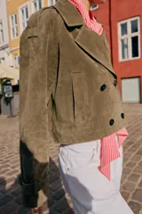 Trench corto de Zara confeccionado en piel de ante, con cuello de solapa, cierre frontal cruzado con botones, mangas largas con trabillas y bolsillos delanteros de vivo.