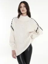 Sweater blanco de tejido grueso con cuello alto y mangas largas con detalle de costuras negras entrecruzadas en los hombros.