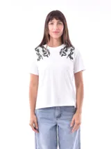 Remera blanca de manga corta con cuello redondo, destacada por apliques bordados con lentejuelas en los hombros.