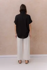 Camisa negra de calce amplio y relajado, confeccionada en tejido liviano con textura sutil. Cuenta con diseño oversize, hombros caídos, mangas cortas amplias, cuello camisero y abotonadura frontal con botones claros.