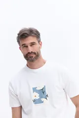 Remera de manga corta color verde menta, con cuello redondo y corte regular. Presenta un estampado frontal con flores blancas sobre un recuadro rectangular de color marrón y el logo de la marca Brooksfield.