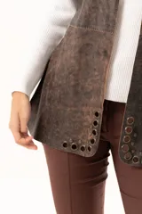 Chaleco de cuero marrón con silueta relajada, caracterizado por detalles de ojalillos metálicos a lo largo de los bordes frontales.