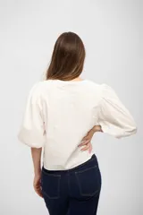 Camisa de algodón color blanco, con cuello redondo, cierre frontal oculto y mangas abullonadas de largo tres cuartos.