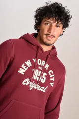 Hoodie bordó con capucha y cordones ajustables, presenta un estampado frontal con texto en color crema y bolsillo tipo canguro.