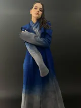 Tapado rojo con capucha, confeccionado en lana merino teñida con técnica tie-dye. Tiene corte recto, largo, bolsillos laterales y cierre cruzado con broches a presión ocultos.