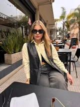 Chaleco de cuero negro, abierto a los costados, con tiras que se regulan a necesidad y gusto de cada una. Presenta bolsillos frontales y escote en V.