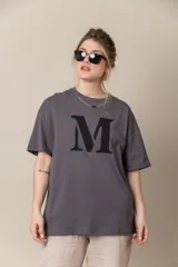 Remera gris con estampa de la letra M en negro y cadena plateada en el cuello.