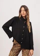 Camisa negra de cuello redondo con frunces y mangas largas con puños abiertos.