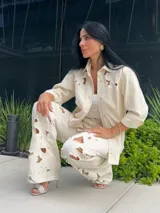 Camisa color off-white con detalles calados en forma de flores en los hombros y cuello. Tiene cierre frontal con botones a presión y cordón decorativo.