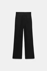 Pantalón negro de tiro alto, con trabillas, bolsillos laterales y de vivo en la espalda. Presenta pliegues en el delantero y cierre frontal con botón.