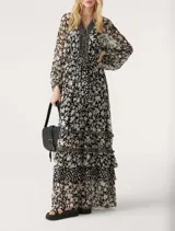 Vestido largo de gasa color negro con estampado floral blanco, escote en V cruzado, mangas largas con aberturas en los hombros y falda con volantes.