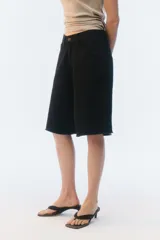 Bermuda oversize de denim color negro, con diseño de cinco bolsillos, cierre de botón y ojal, y ruedo deshilachado.