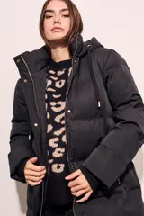 Tapado negro largo con capucha, diseño capitoneado y cierre frontal con botones dorados.