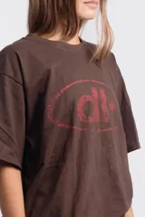 Remera de corte holgado color marrón chocolate, con cuello redondo y mangas cortas. Presenta un estampado frontal en color rojo con un diseño de elipse y una estrella.