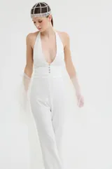 Mono largo de color blanco con diseño elegante, cuerpo entallado y mangas largas de tul con volados en los hombros. Presenta un pantalón de corte recto y fluido.