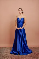 Vestido largo de fiesta color azul eléctrico, strapless, con escote corazón y detalle de piedras brillantes en el borde superior. Tiene corte imperio con falda amplia y plisada.