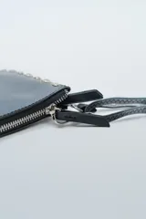 Cartera negra de cuero sintético con tachas metálicas plateadas en los bordes y cierre superior. Incluye correa larga ajustable.