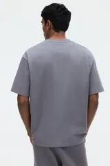 Remera gris de corte relajado, confeccionada en punto liviano con cuello redondo ribeteado, hombros caídos y mangas cortas.