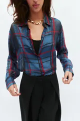 Camisa de manga larga con cuello solapa y cierre frontal con botones. Presenta un diseño de cuadros en tonos azules y rojos sobre un tejido semitransparente.