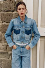 Cazadora corta de denim con cuello solapa y manga larga. Presenta un diseño de lavado combinado a contraste, con bolsillos de plastrón con solapa en el pecho y cierre frontal con botones metálicos.