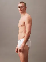 Pack de tres slips Calvin Klein de tiro medio, corte hip brief, confeccionados en algodón elástico con tecnología que elimina la humedad. Presentan cinturillas elásticas blancas con el logo de la marca repetido en negro.