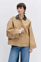 Cazadora de corte oversize en color beige, con cuello de solapa en contraste de color oscuro, cierre frontal con botones y bolsillos laterales.